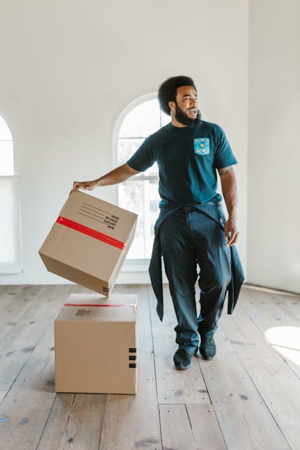Two movers from Self Storage Uxbridge are engaged in a home relocation process, carefully loading a large, dark green upholstered furniture piece into the open rear cargo space of a white delivery van